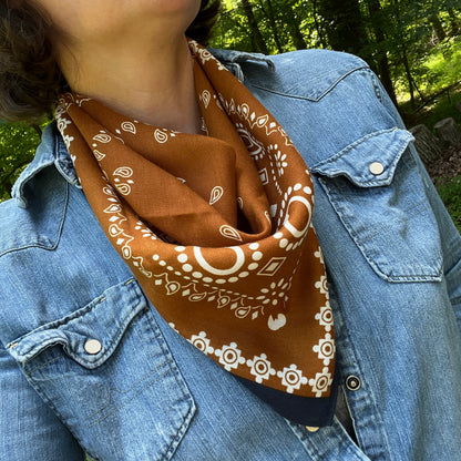 Person wearing a brown bandana with white patterns over a blue denim jacket outdoors.
