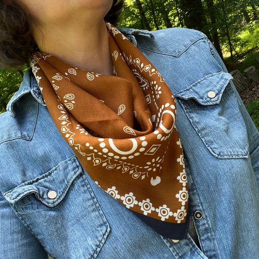 Person wearing a brown bandana with white patterns over a blue denim jacket outdoors.