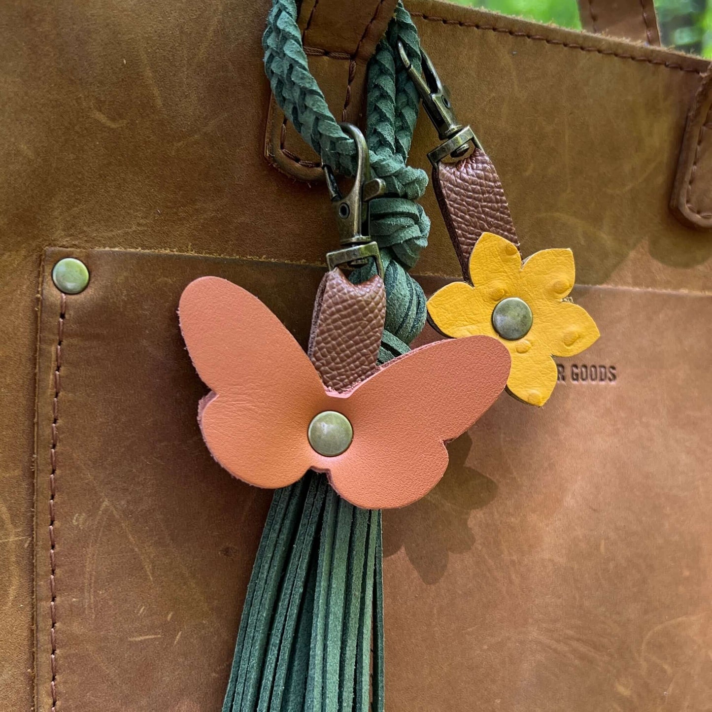 Butterfly and flower keychain attached to a brown leather bag.