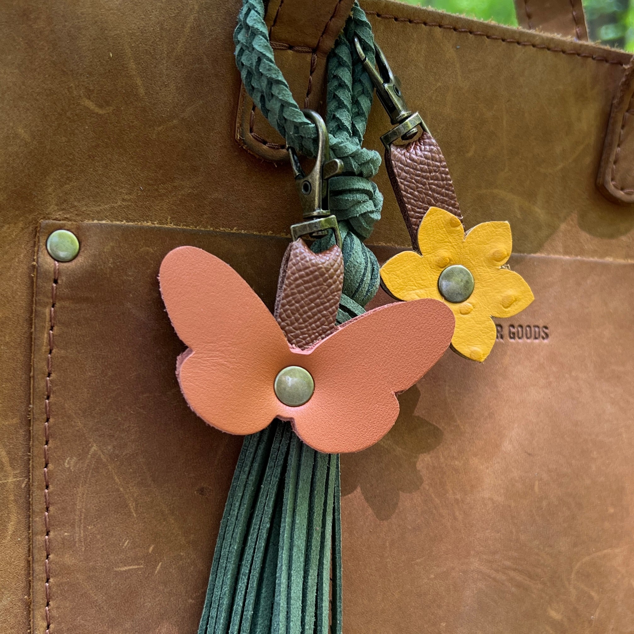 Butterfly and flower keychain attached to a brown leather bag.