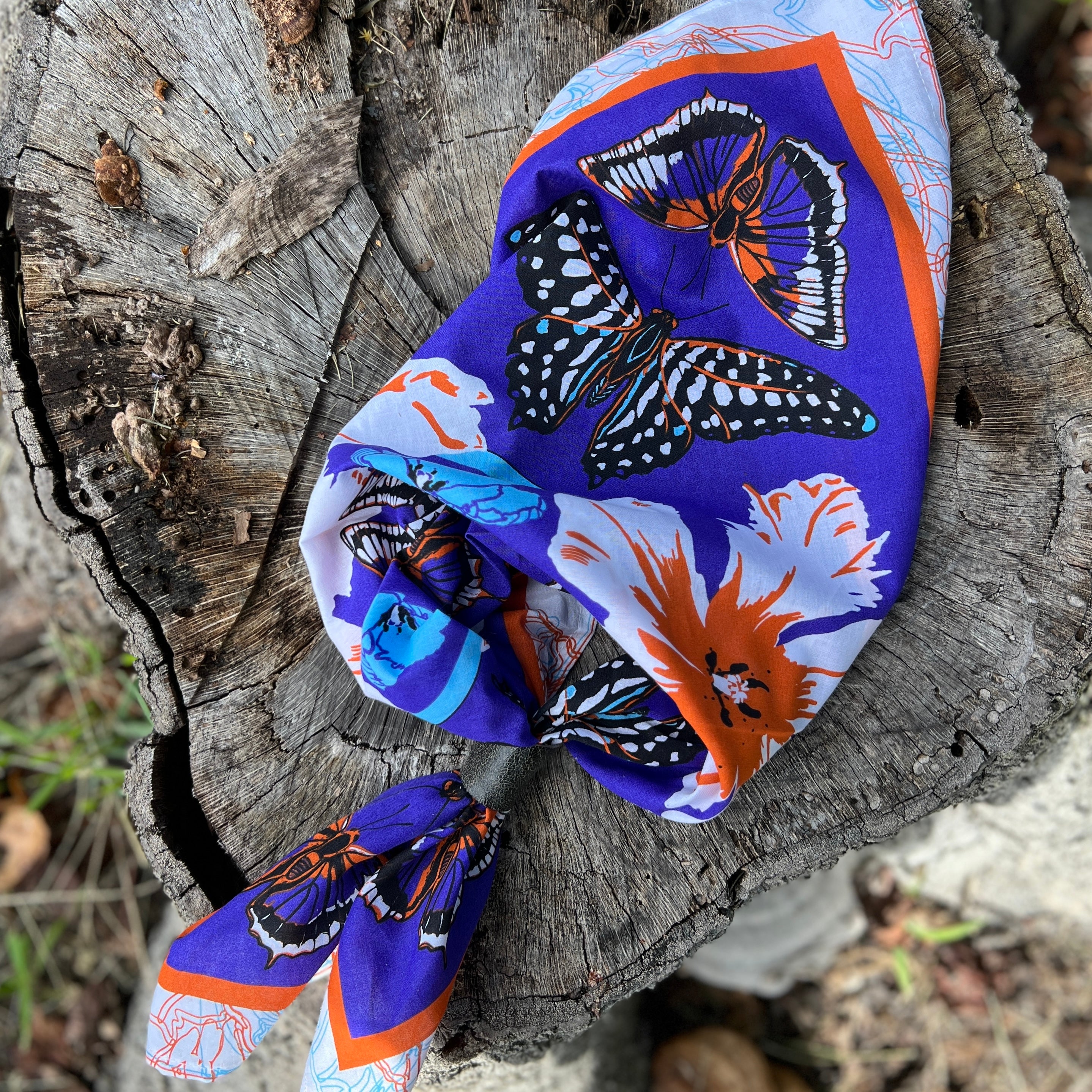 Colorful butterfly-patterned headscarf on a wooden log