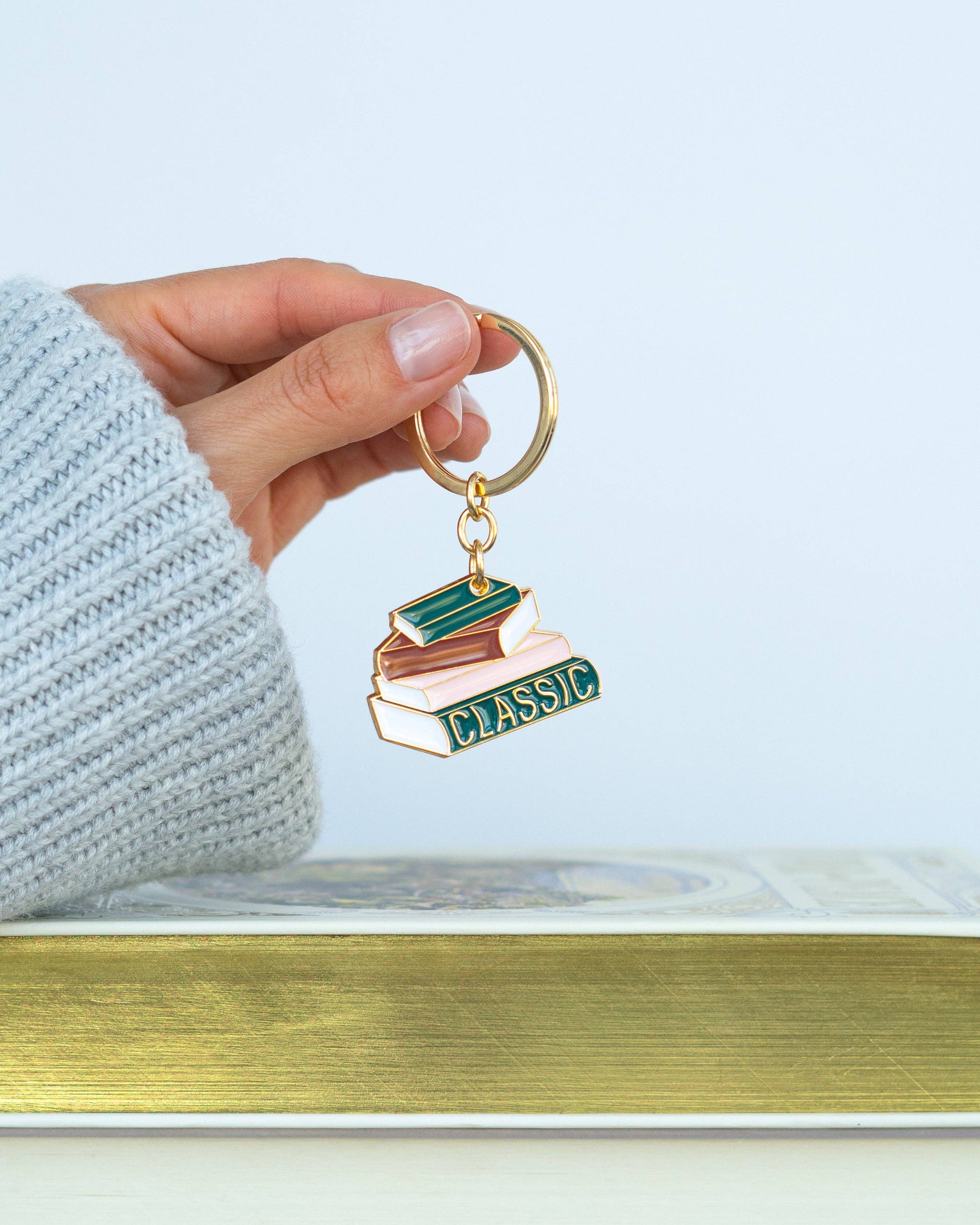 Hand holding a keychain with book design and 'classic' text against a light background