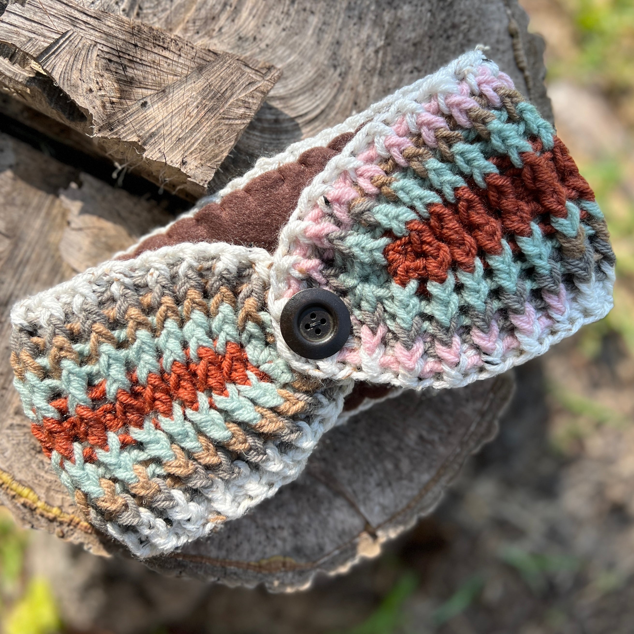 Crocheted headband with button closure on a wooden log