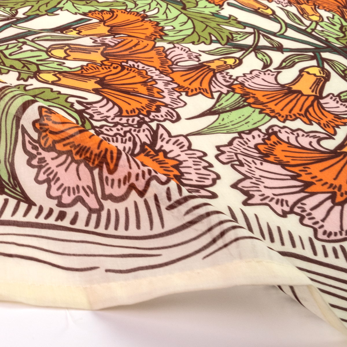 A close-up of a printed textile or scarf with a botanical pattern featuring orange flowers, pink and green leaves, and brown linework on an off-white background.