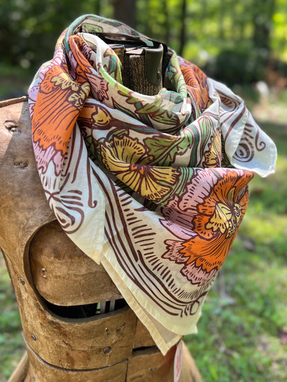 A multicolor floral scarf with orange, green, pink, and brown patterns on a cream base, draped over a rustic wooden armor display outdoors.