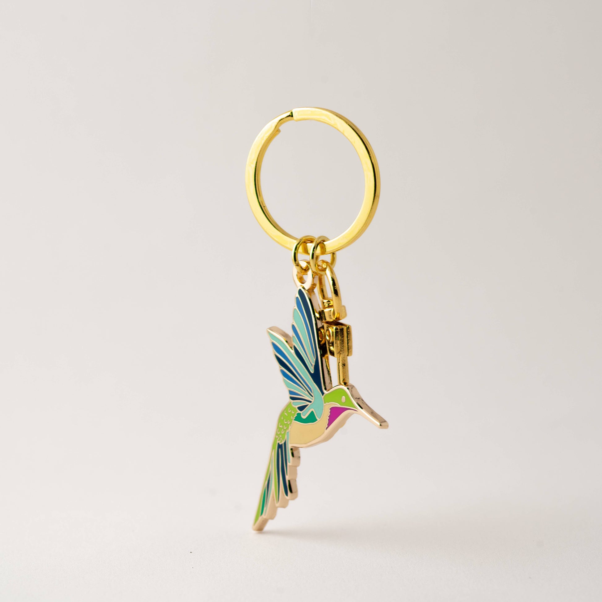 Gold keychain with a colorful hummingbird charm on a light gray background