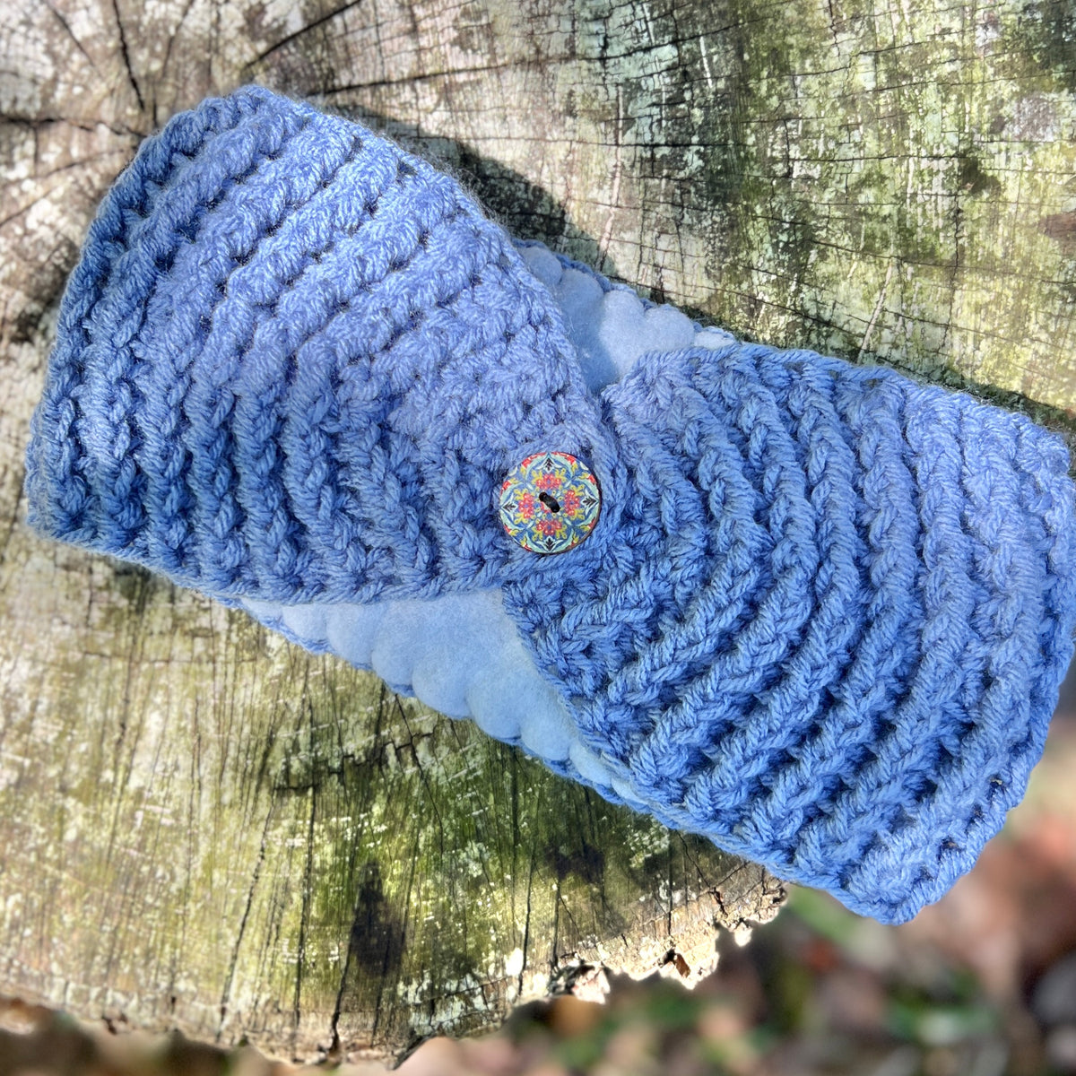 denim blue ear warmer winter headband with fleece lining and colorful button on wooden surface
