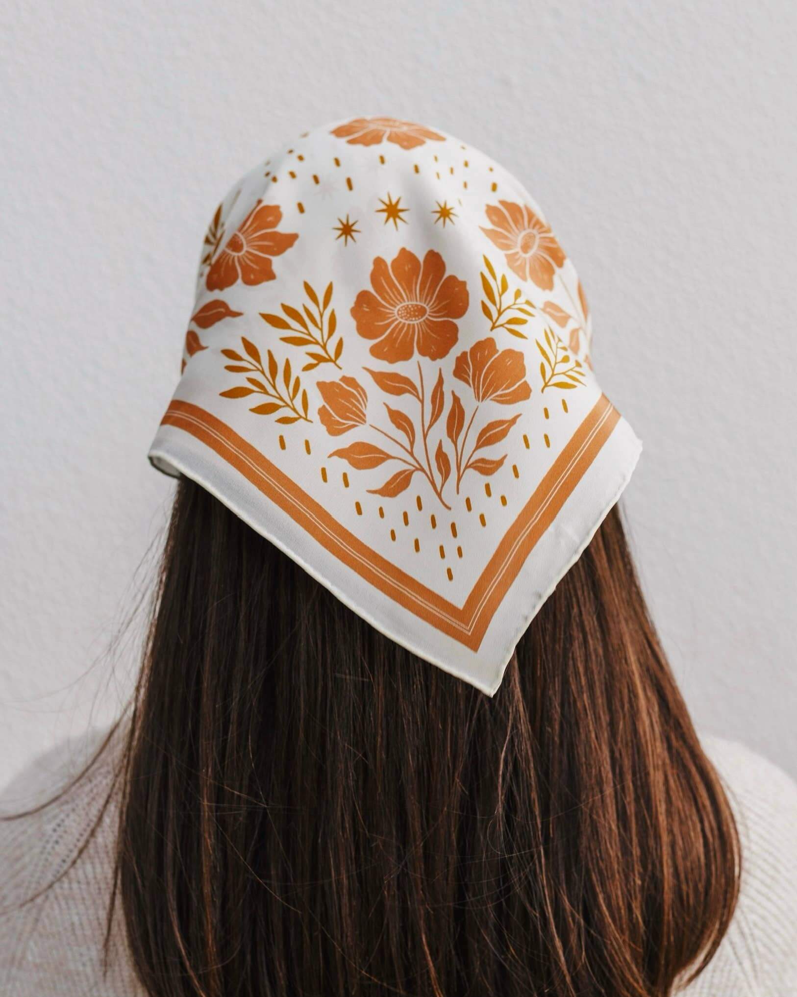 Person wearing a white headscarf with orange floral patterns on a plain background