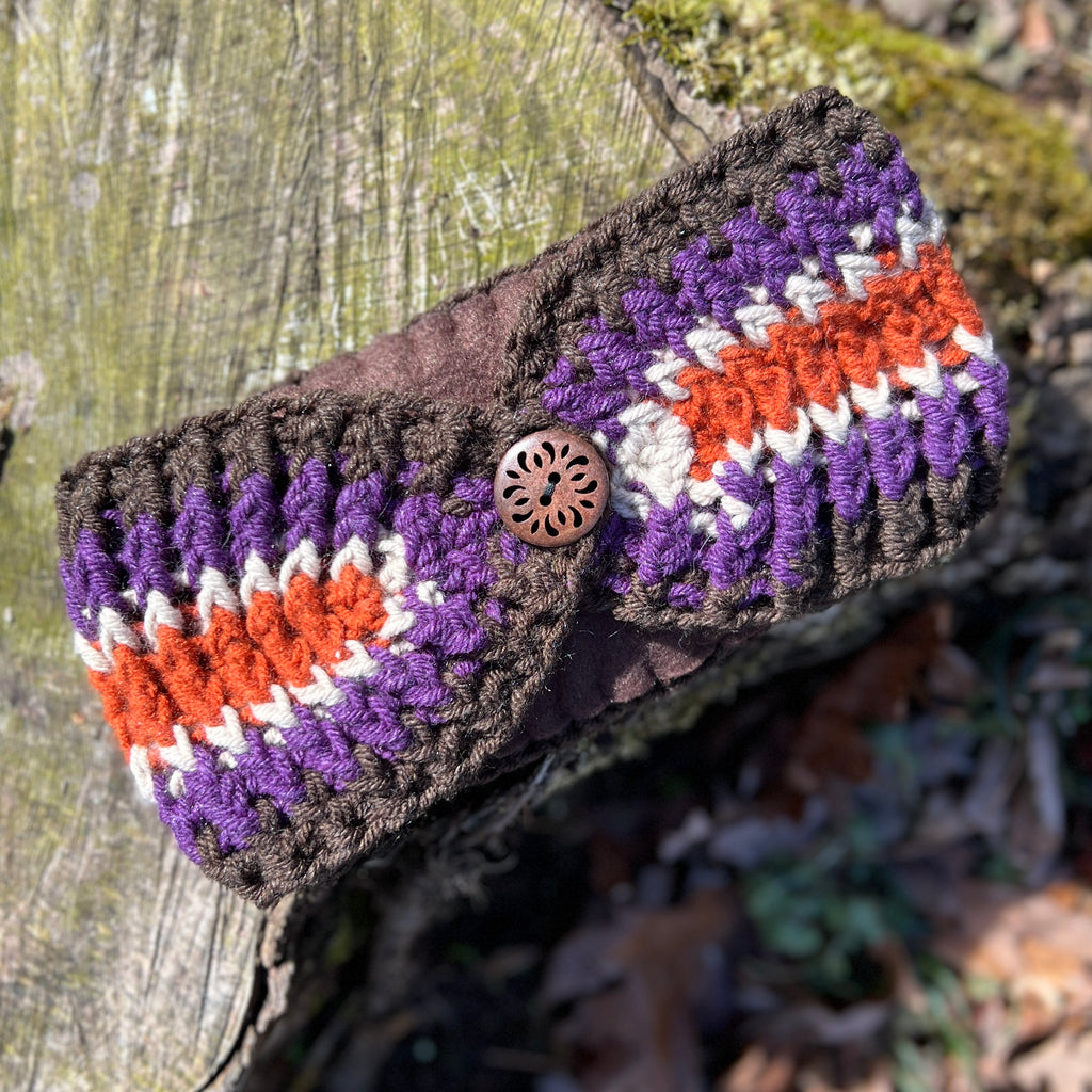 Crocheted headband with purple, orange, and white pattern on a wooden surface