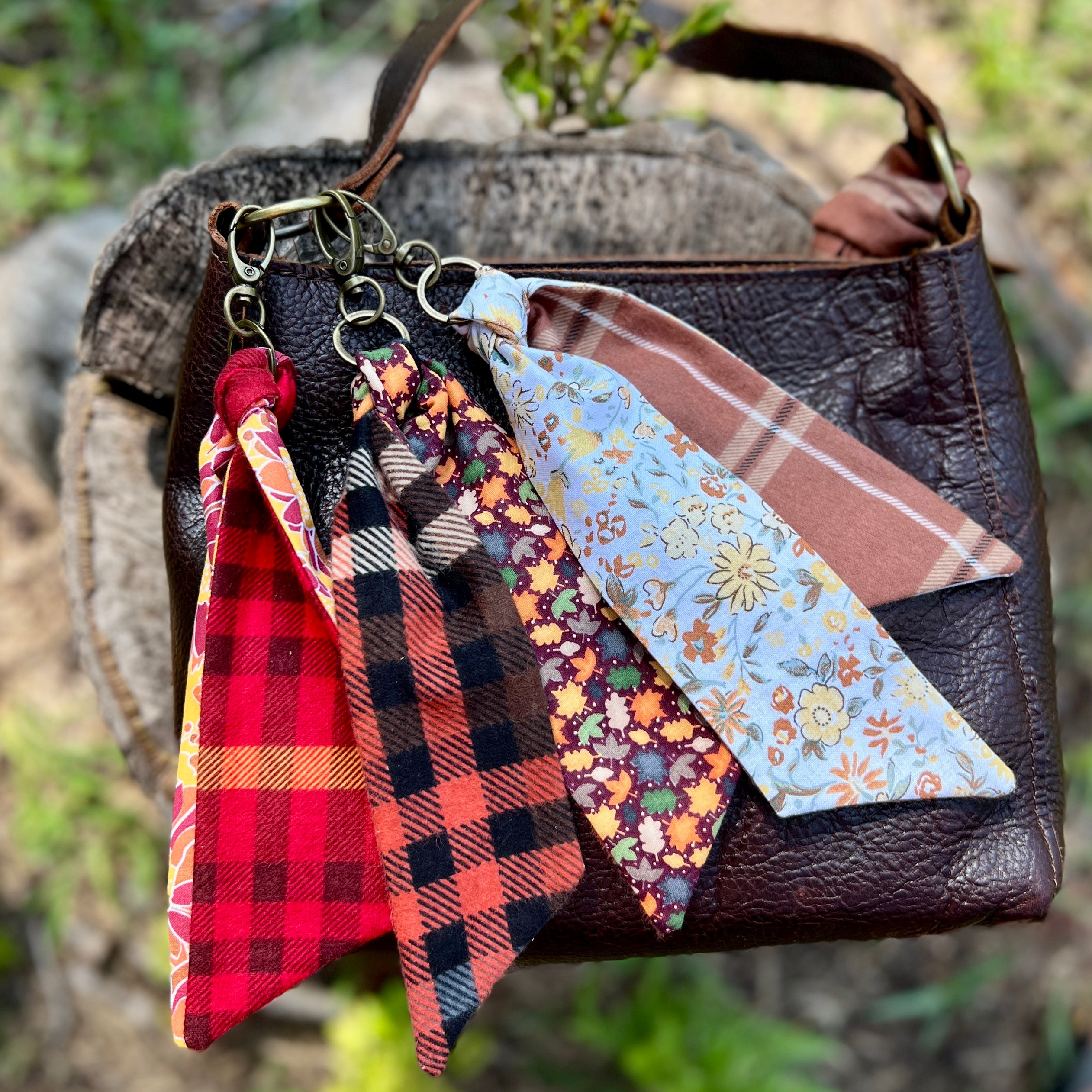 Collection of fabric keychains on a brown leather bag with a natural background