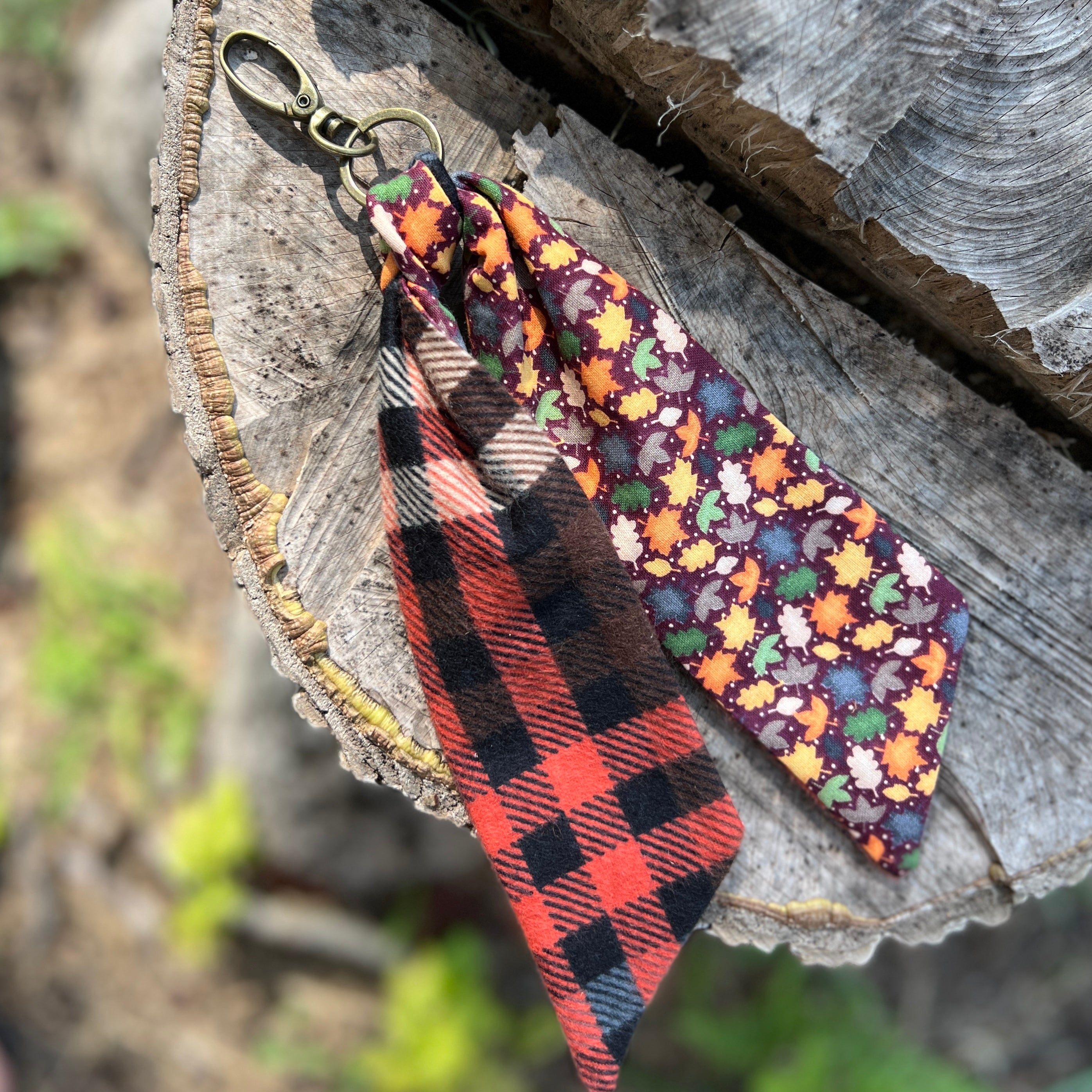 Two fabric keychains, one plaid and one with autumn leaf pattern, on a wooden surface.