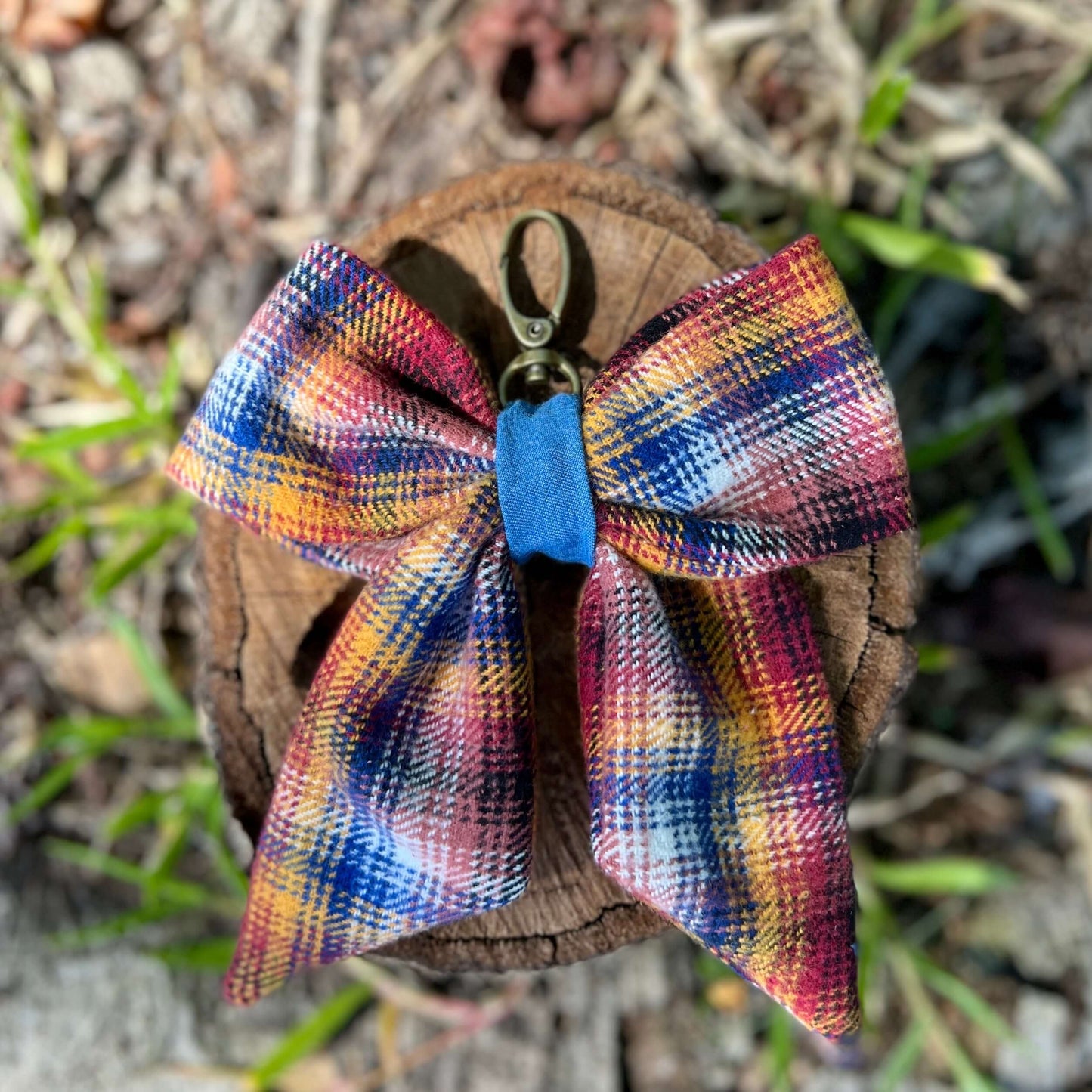 Colorful plaid bow keychain on a wooden surface with grass in the background