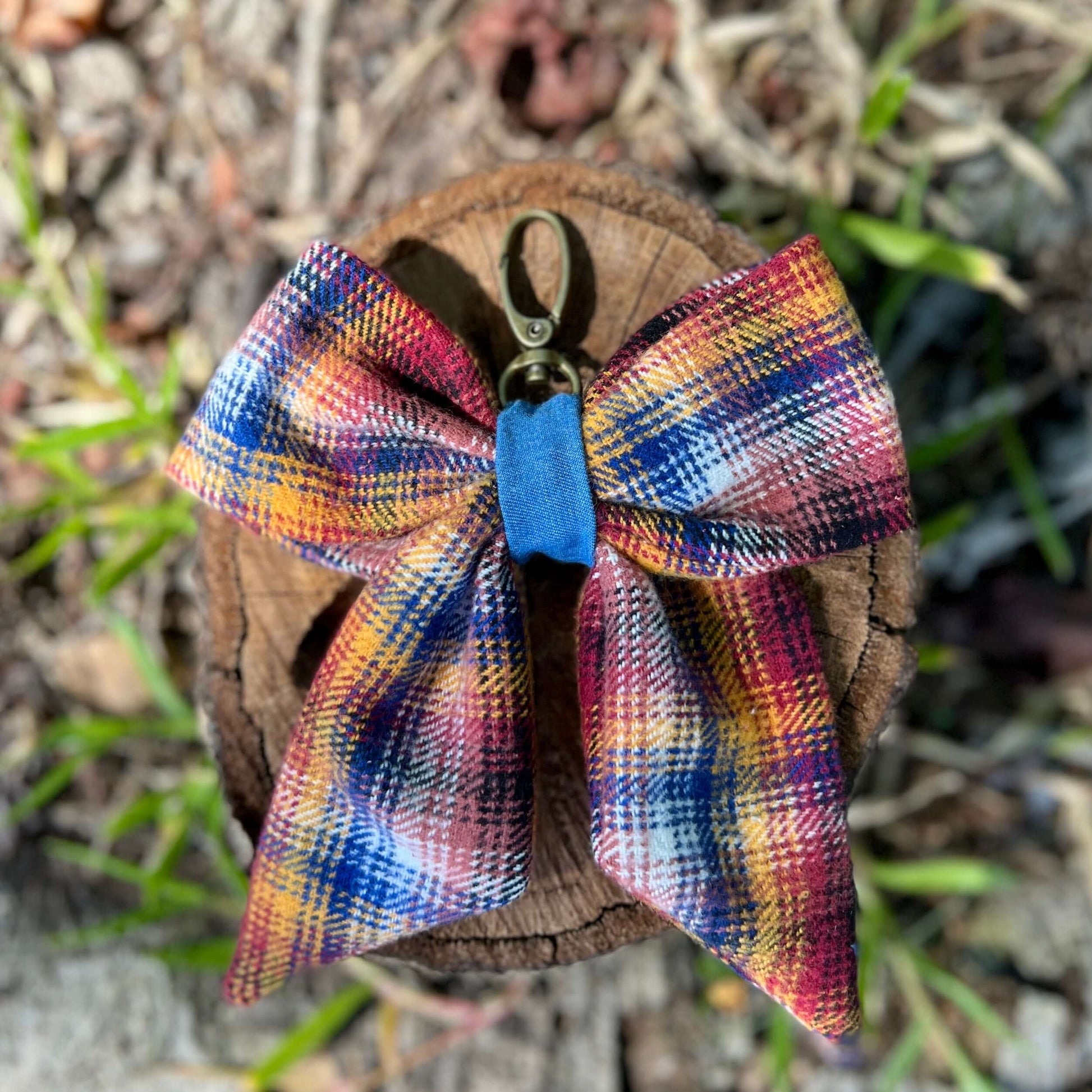 Colorful plaid bow keychain on a wooden surface with grass in the background