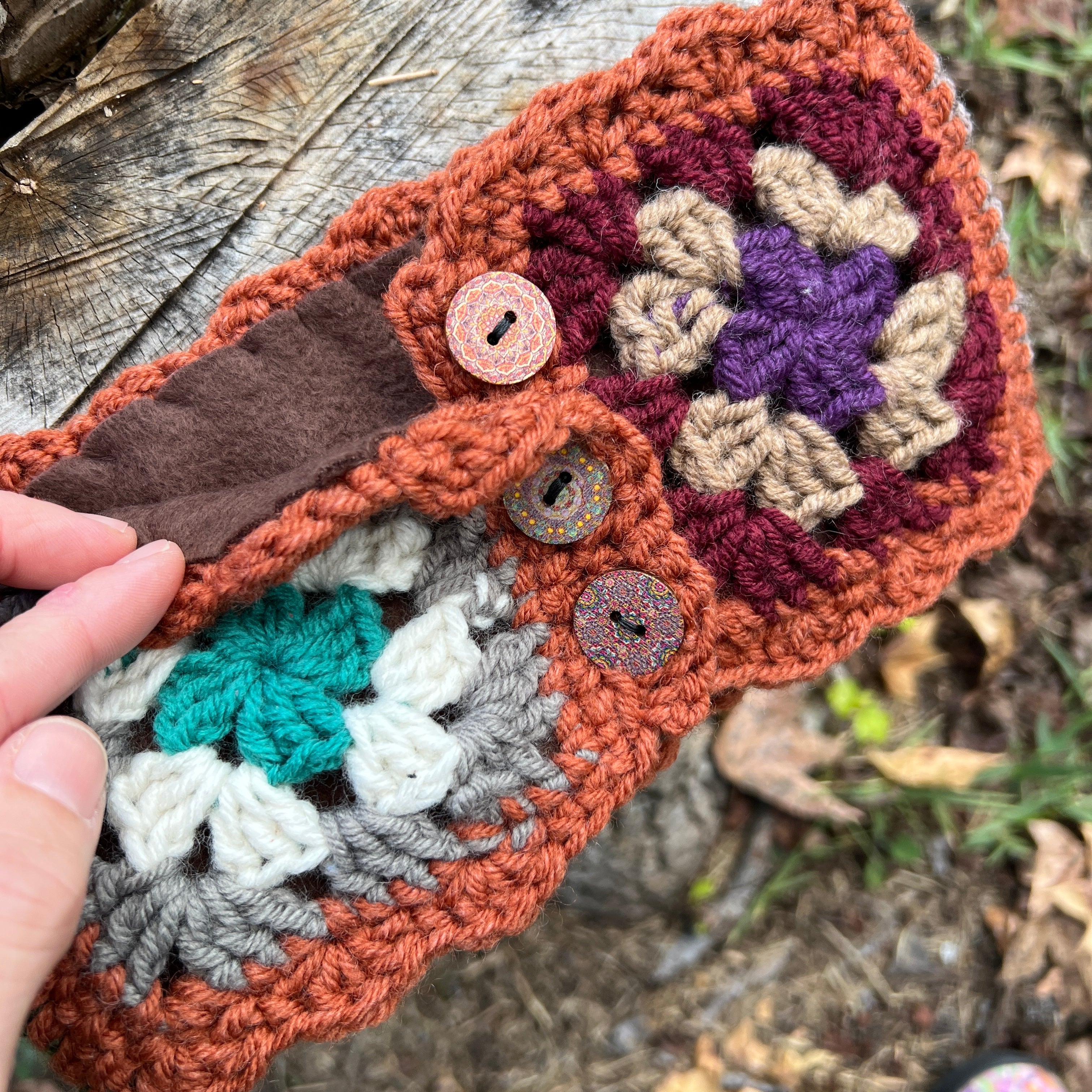 Crocheted headband with colorful flower patterns and buttons on a wooden surface.