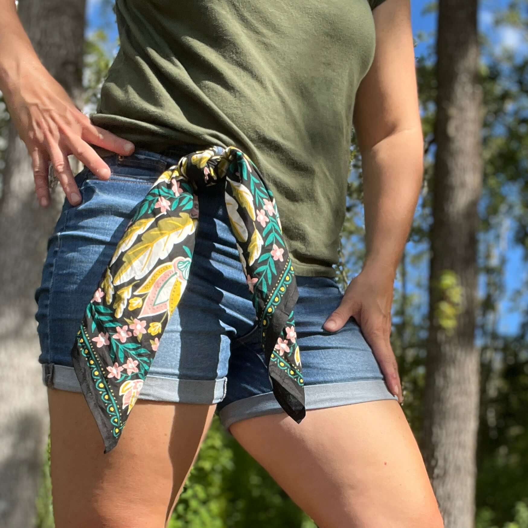 Person wearing a green shirt and blue shorts with a floral scarf tied around their waist, standing outdoors.
