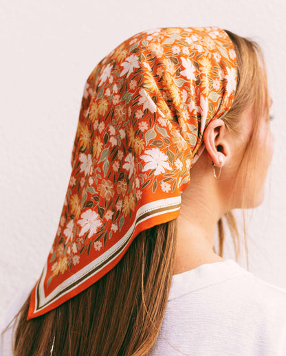 Woman wearing a floral headscarf with orange, white, and green colors on a plain background