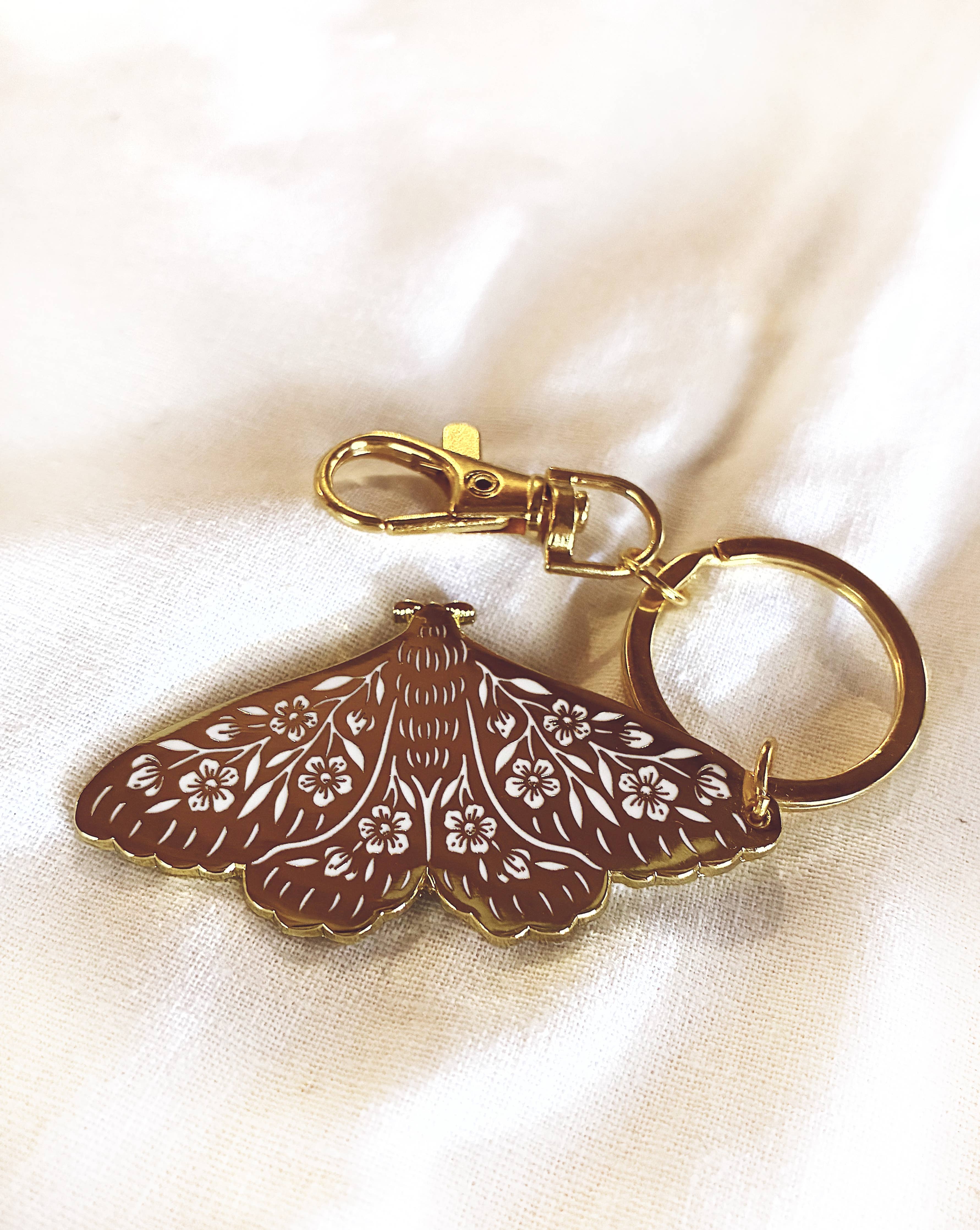 Decorative keychain with moth design on a beige fabric background
