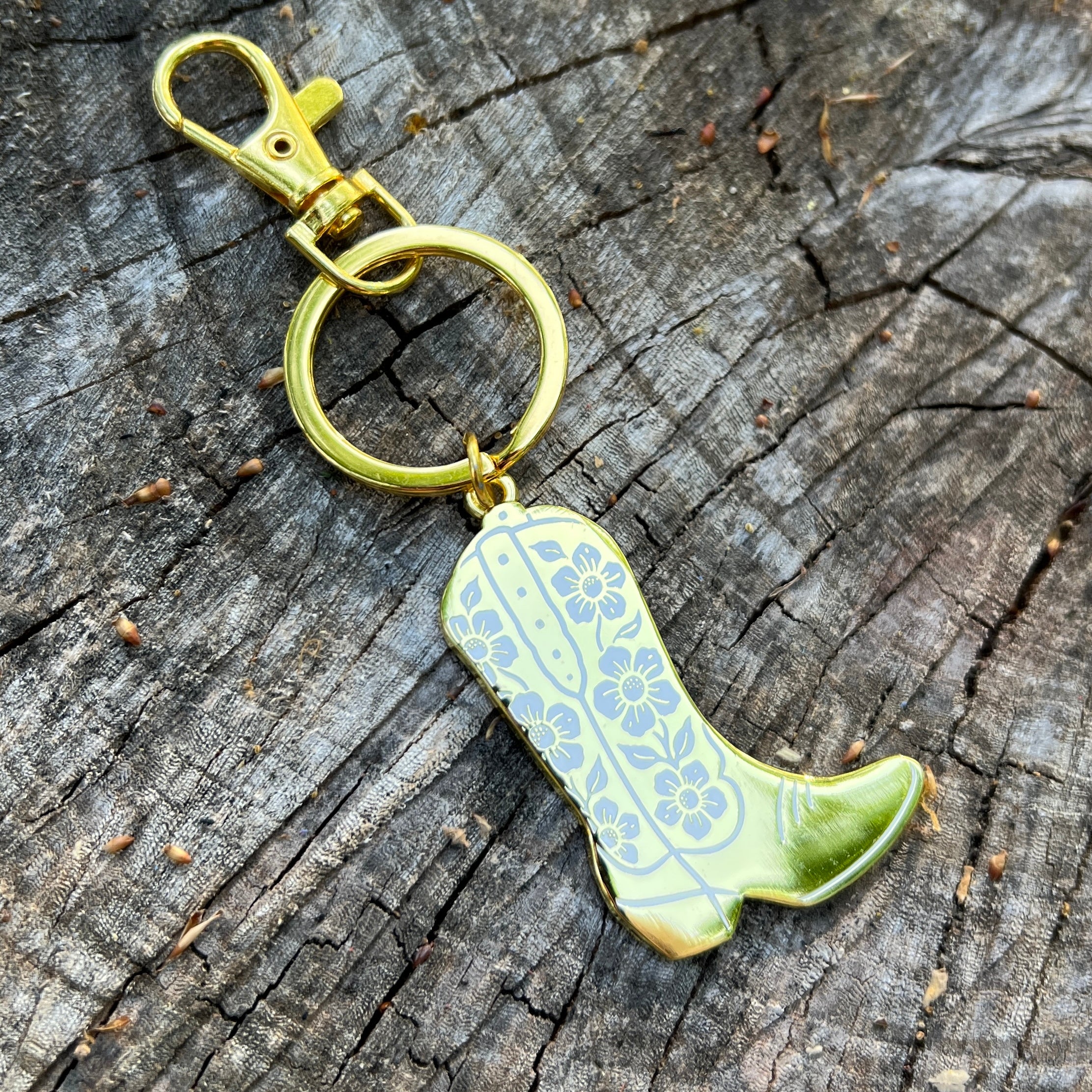 Gold boot-shaped key chain with floral patterns on a wooden surface