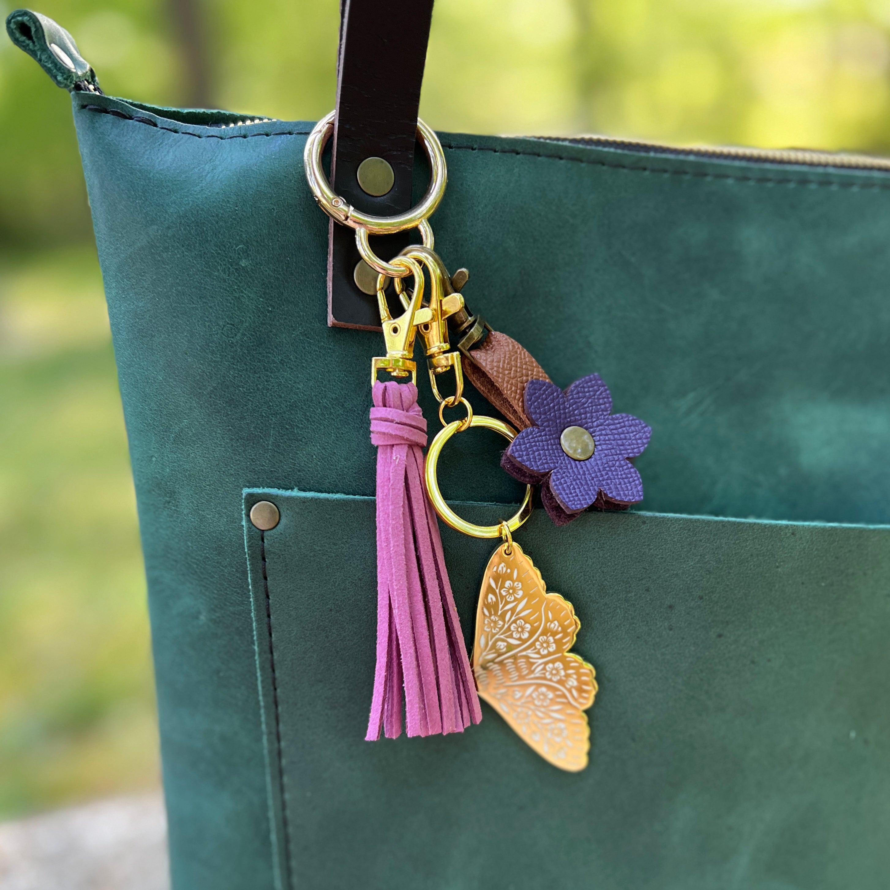 Keychain with butterfly and flower charm attached to a green bag outdoors