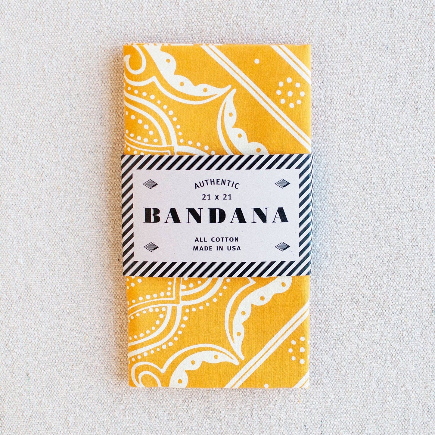 Yellow bandana with white patterns in a packaging sleeve on a light gray background