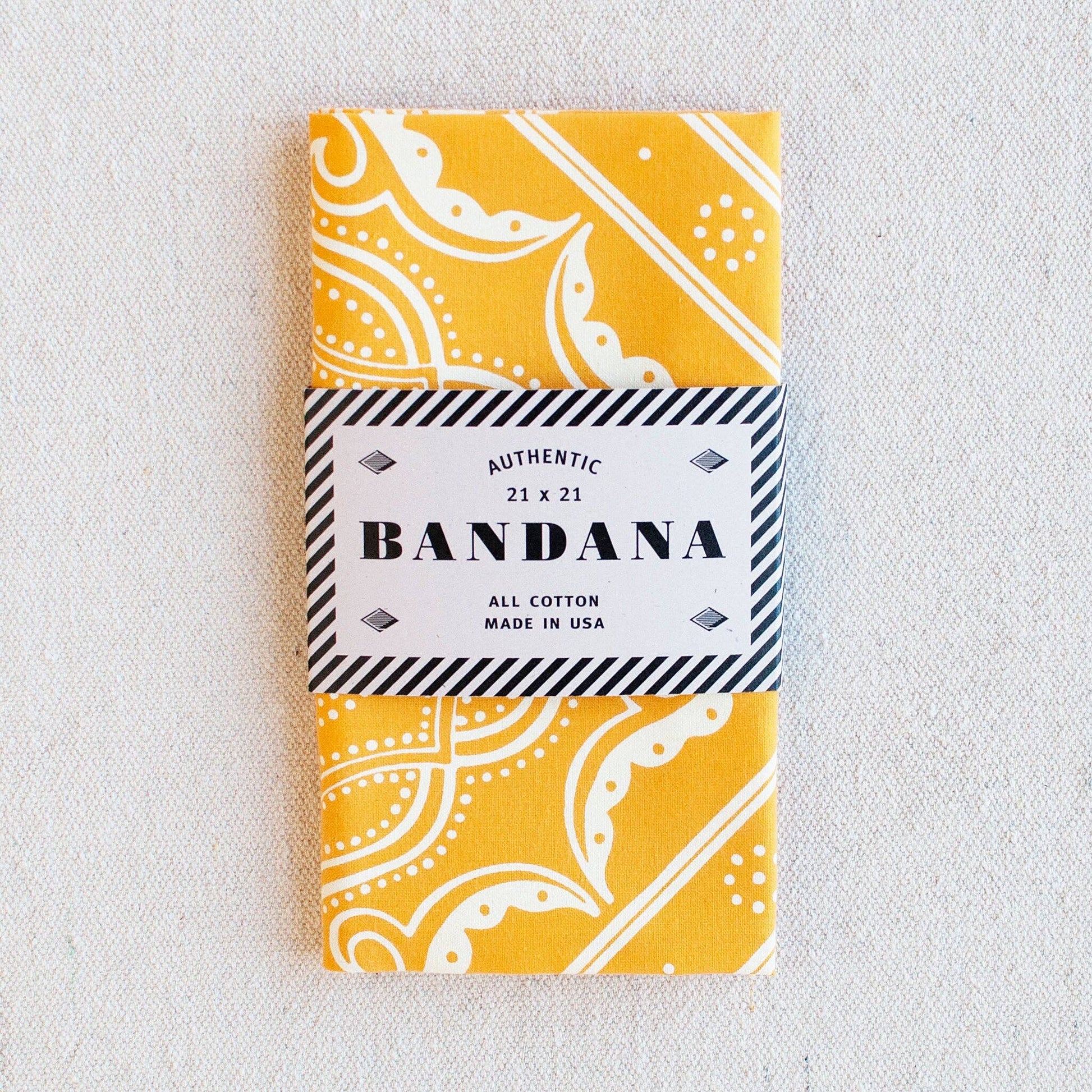 Yellow bandana with white patterns in a packaging sleeve on a light gray background