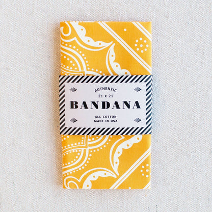 Yellow bandana with white patterns in a packaging sleeve on a light gray background