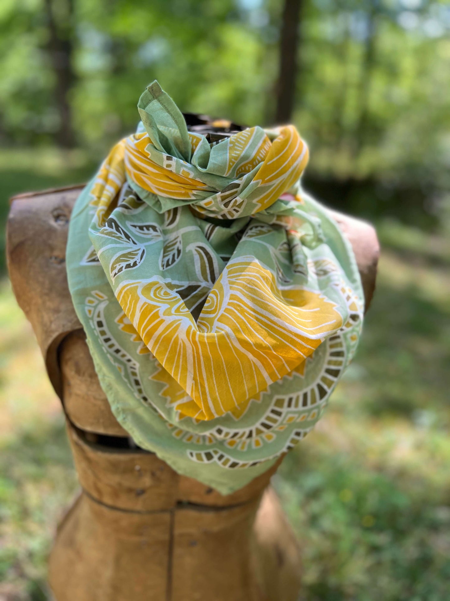 Green and yellow patterned headscarf on a wooden mannequin with a blurred natural background