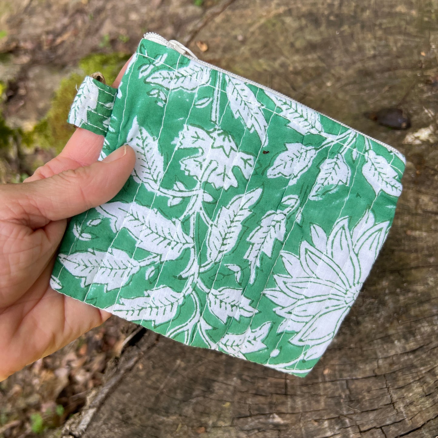 Hand holding a green fabric pouch with white leaf pattern on a wooden surface