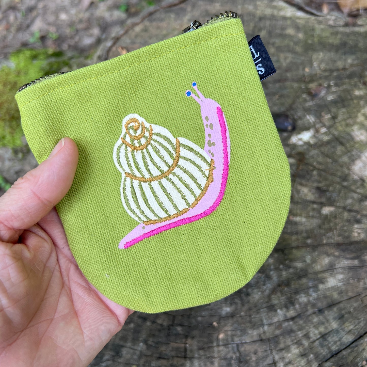 Green pouch with a snail design held by a hand on a wooden surface