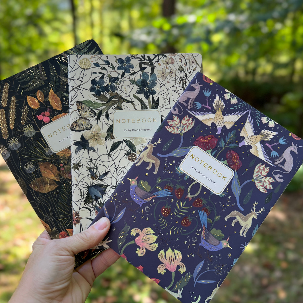 hand holding floral notebooks with forest background