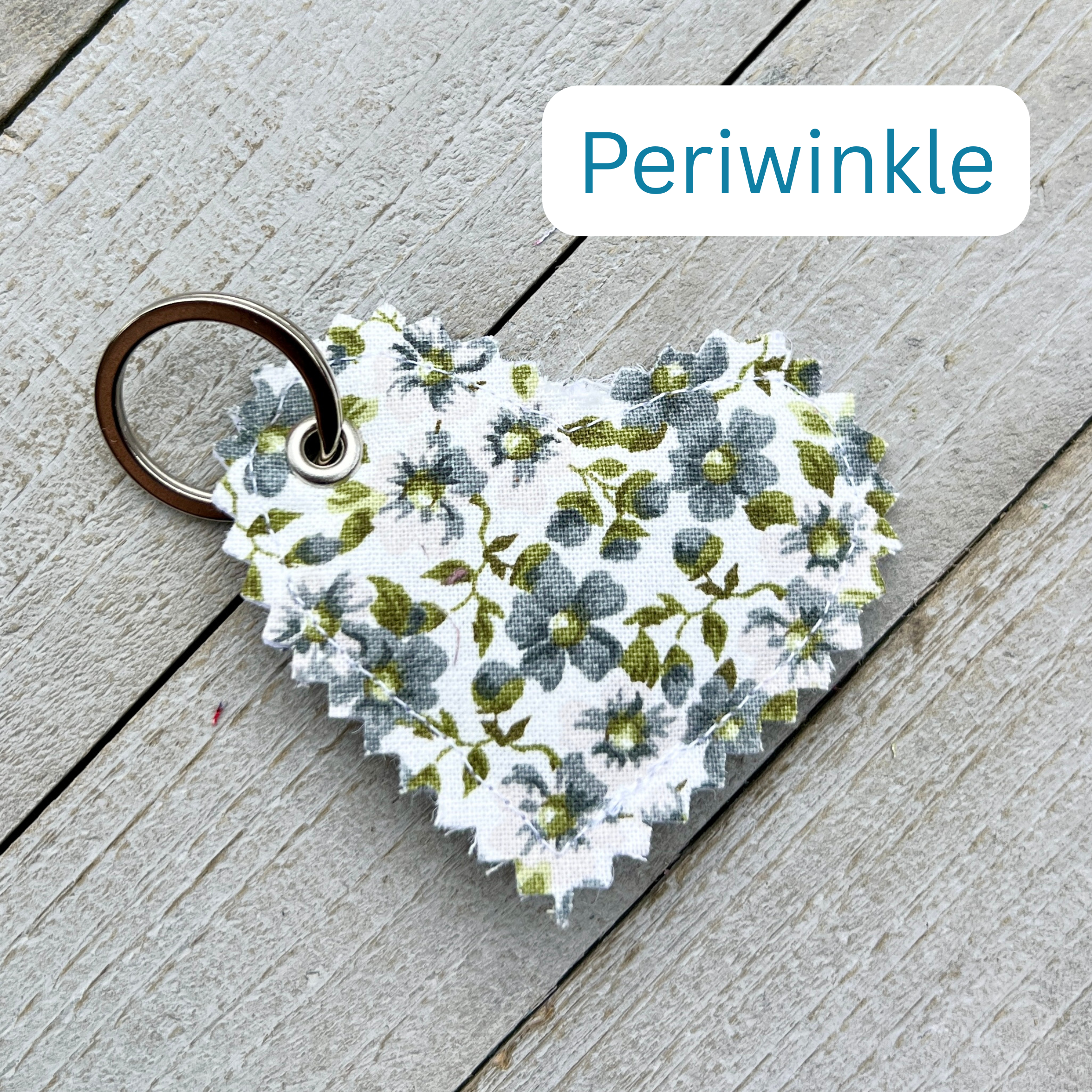 Heart-shaped keychain with floral pattern on a wooden surface, labeled 'Periwinkle'.
