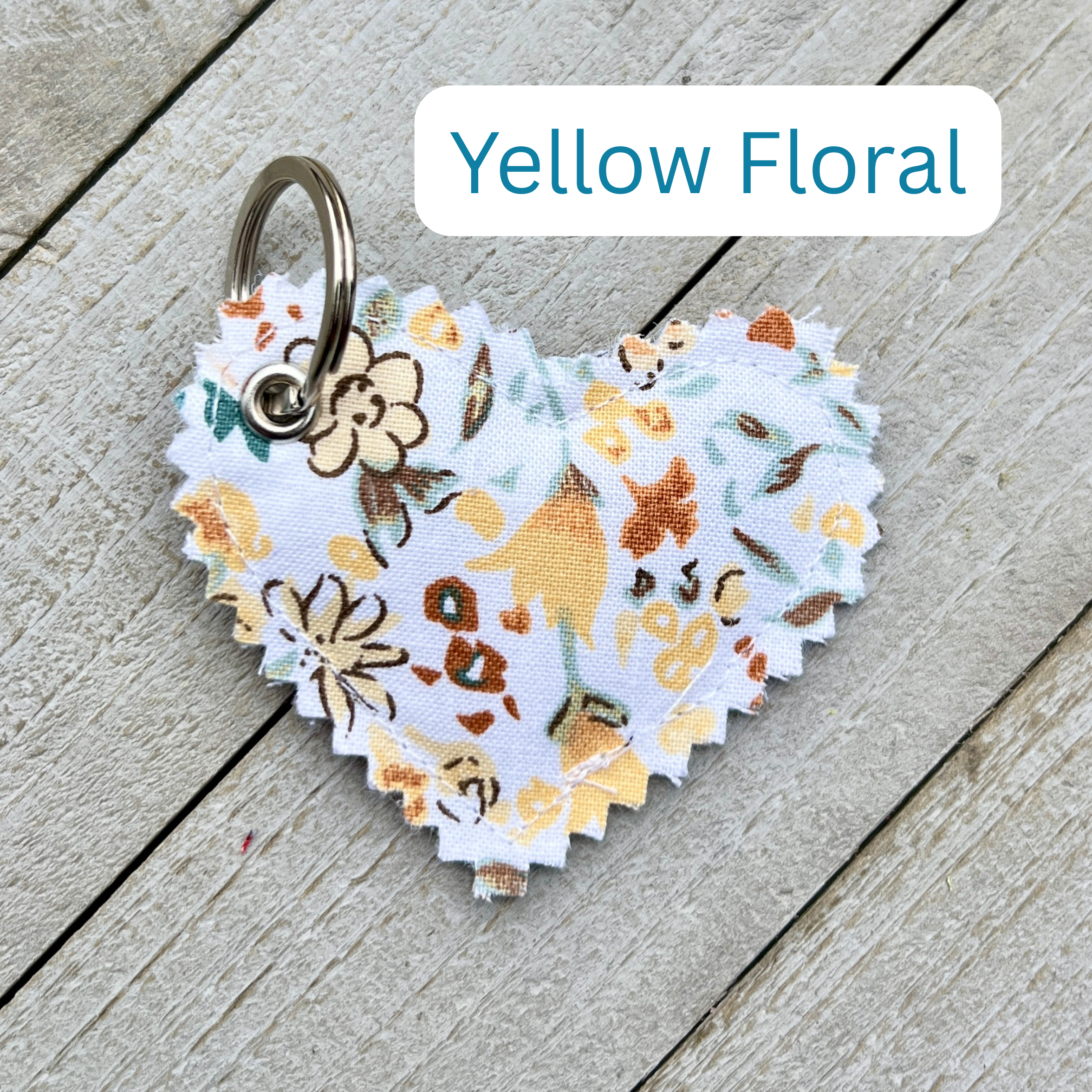 Heart-shaped keychain with yellow floral pattern on a wooden surface