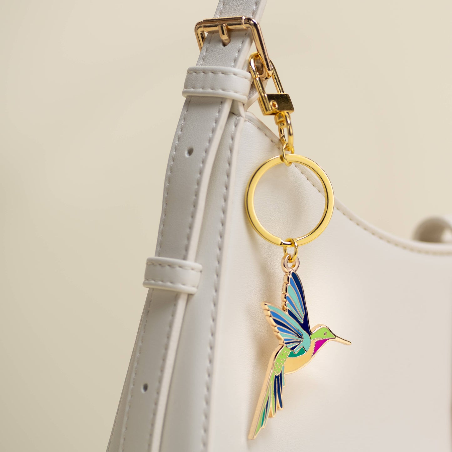 Colorful hummingbird keychain attached to a white strap with a beige background