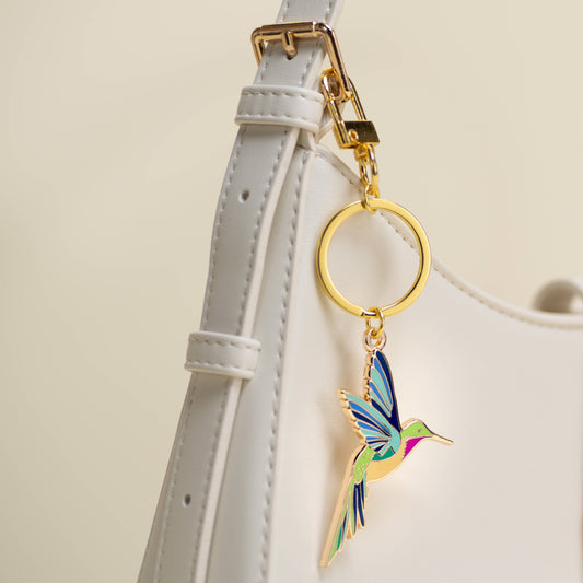 Colorful hummingbird keychain attached to a white strap with a beige background