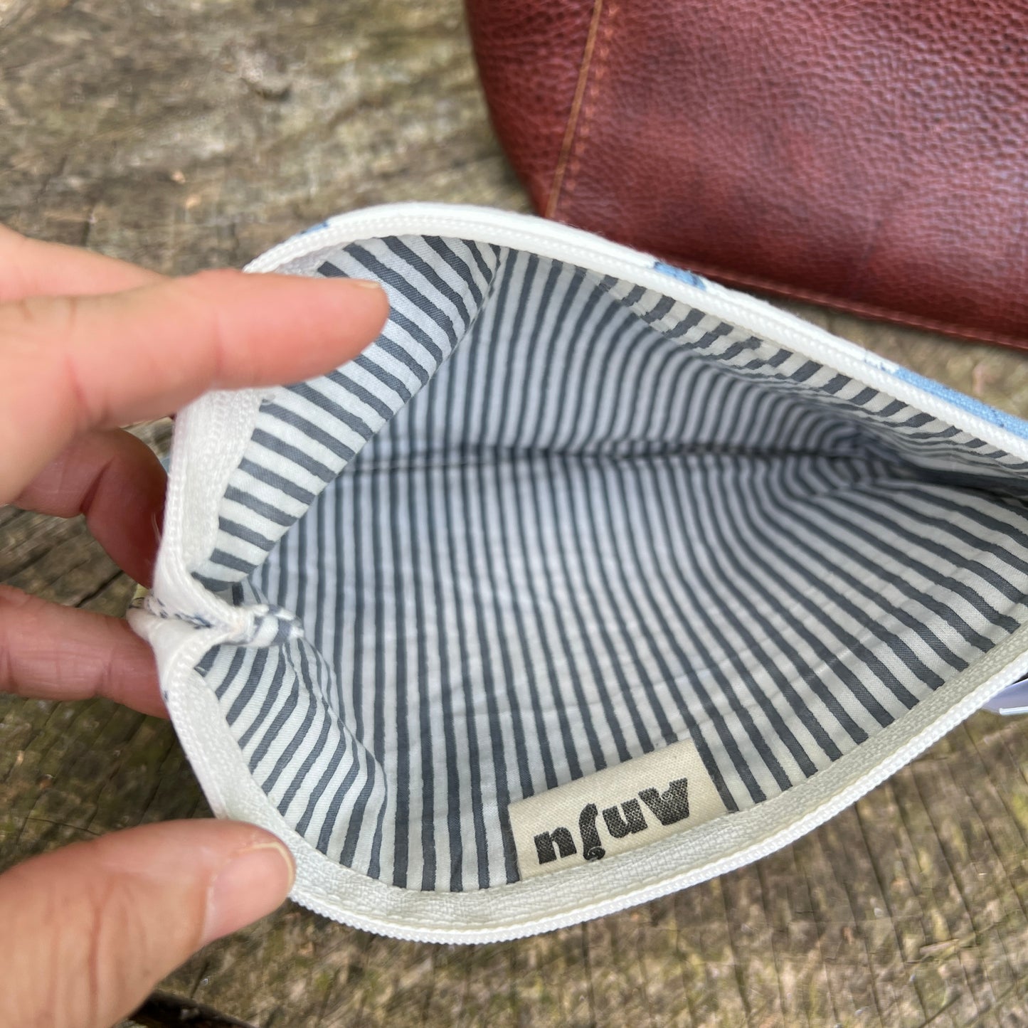 Striped fabric lining of a product with 'Anju' branding, held by a hand on a wooden surface.