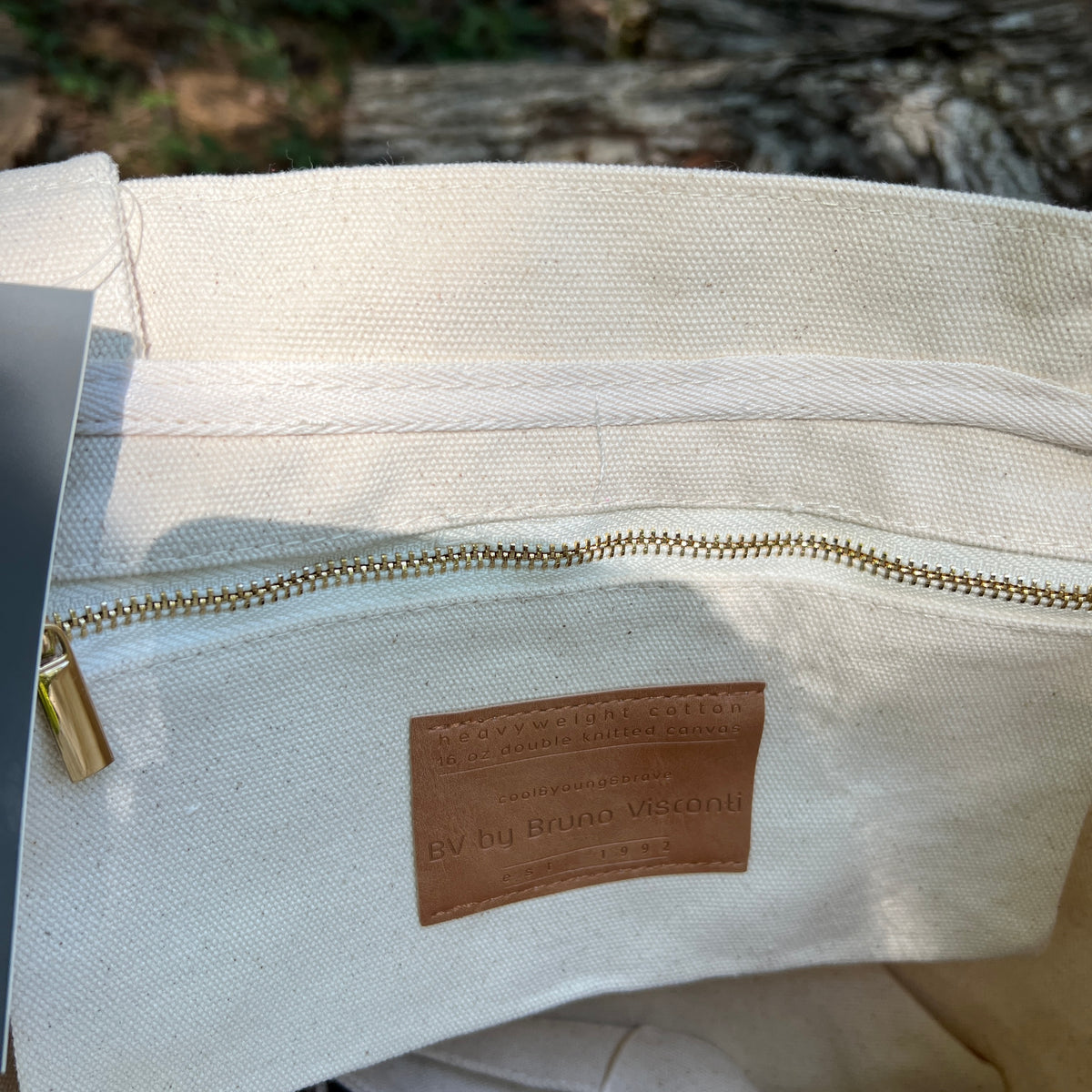 Close-up of a canvas tote bag interior showing a brass zipper, a tan leather brand patch 