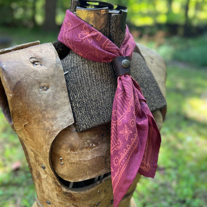 A maroon red bandana with a tan western-style star pattern, styled on a medieval-style wooden armor mannequin torso outdoors.