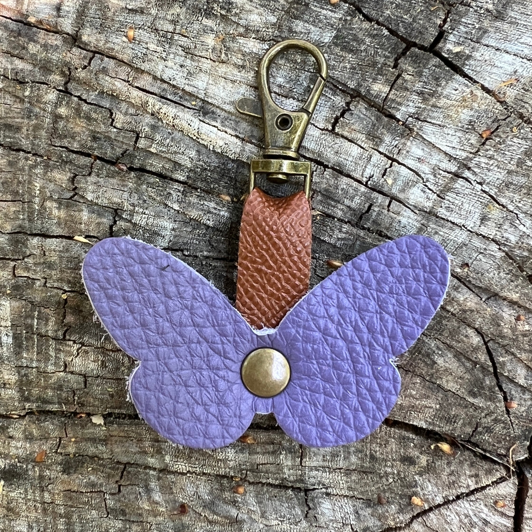 Butterfly-shaped keychain with purple body and brown strap on a wooden surface