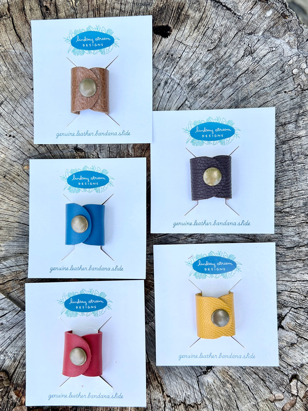 Set of four genuine leather bandana slides on display cards against a wooden background.