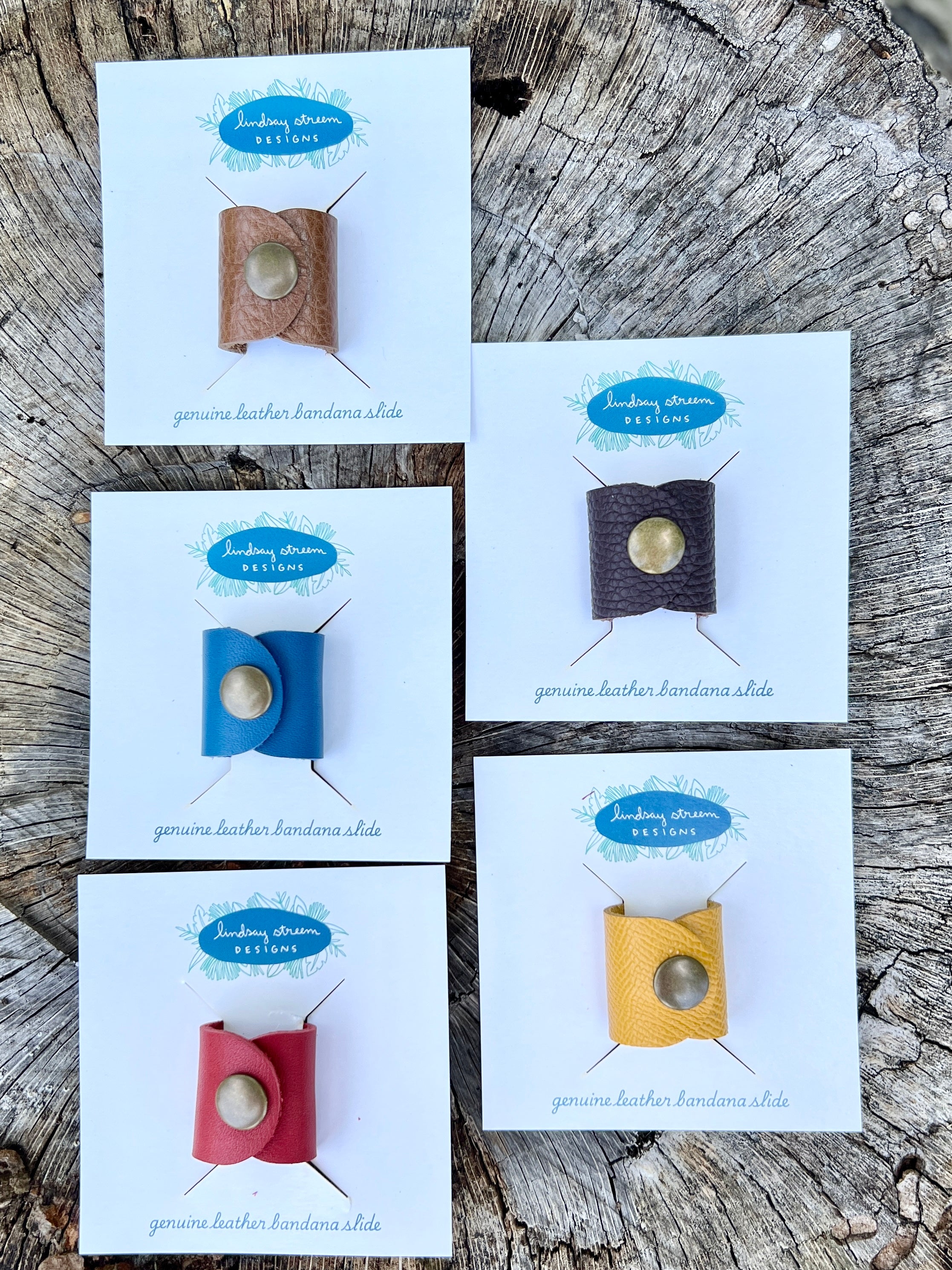 Set of four genuine leather bandana slides on display cards against a wooden background.