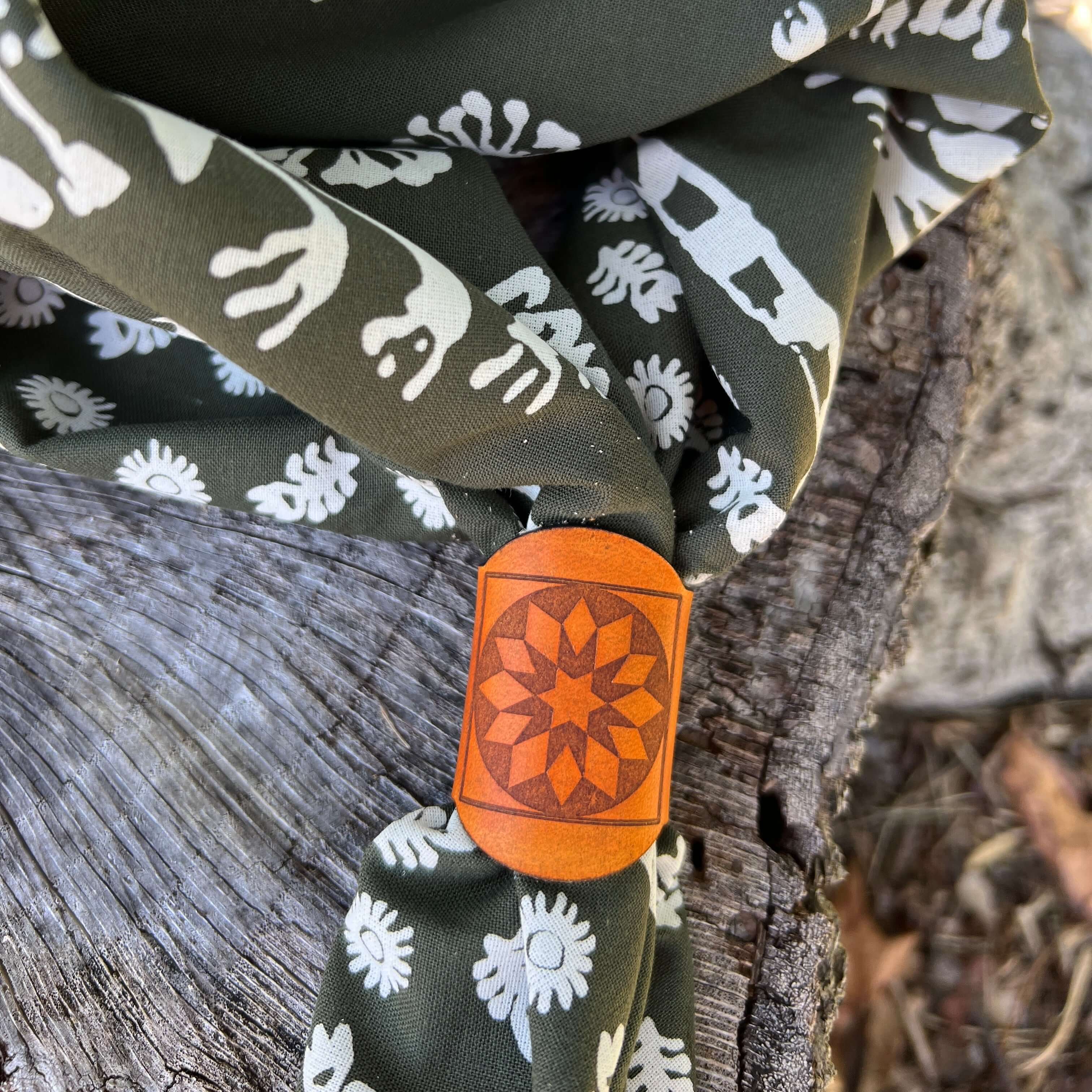 Green fabric with white patterns and a leather bandana slide on a wooden surface