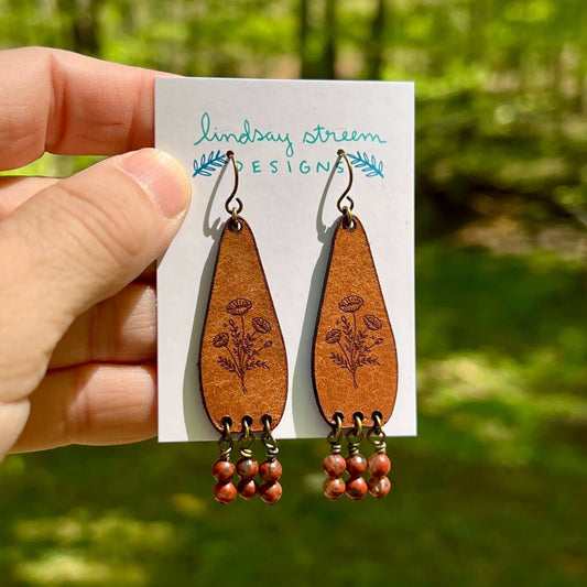 Wooden earrings with floral designs on a card held by a hand against a natural background