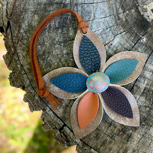 Decorative leather flower pendant with brown, blue, and beige colors on a wooden surface.