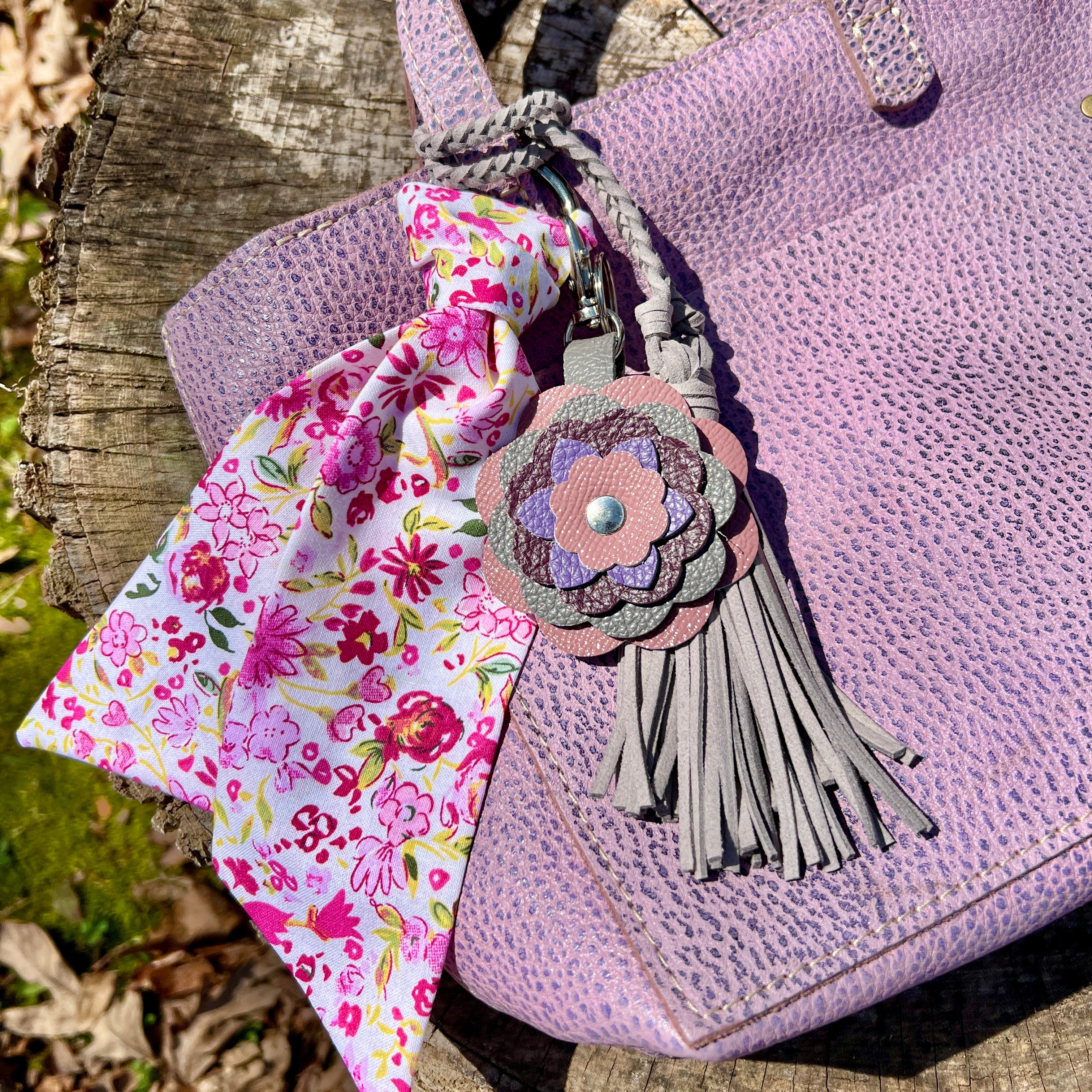 Purple textured bag with a floral keychain and tassel on a wooden surface.