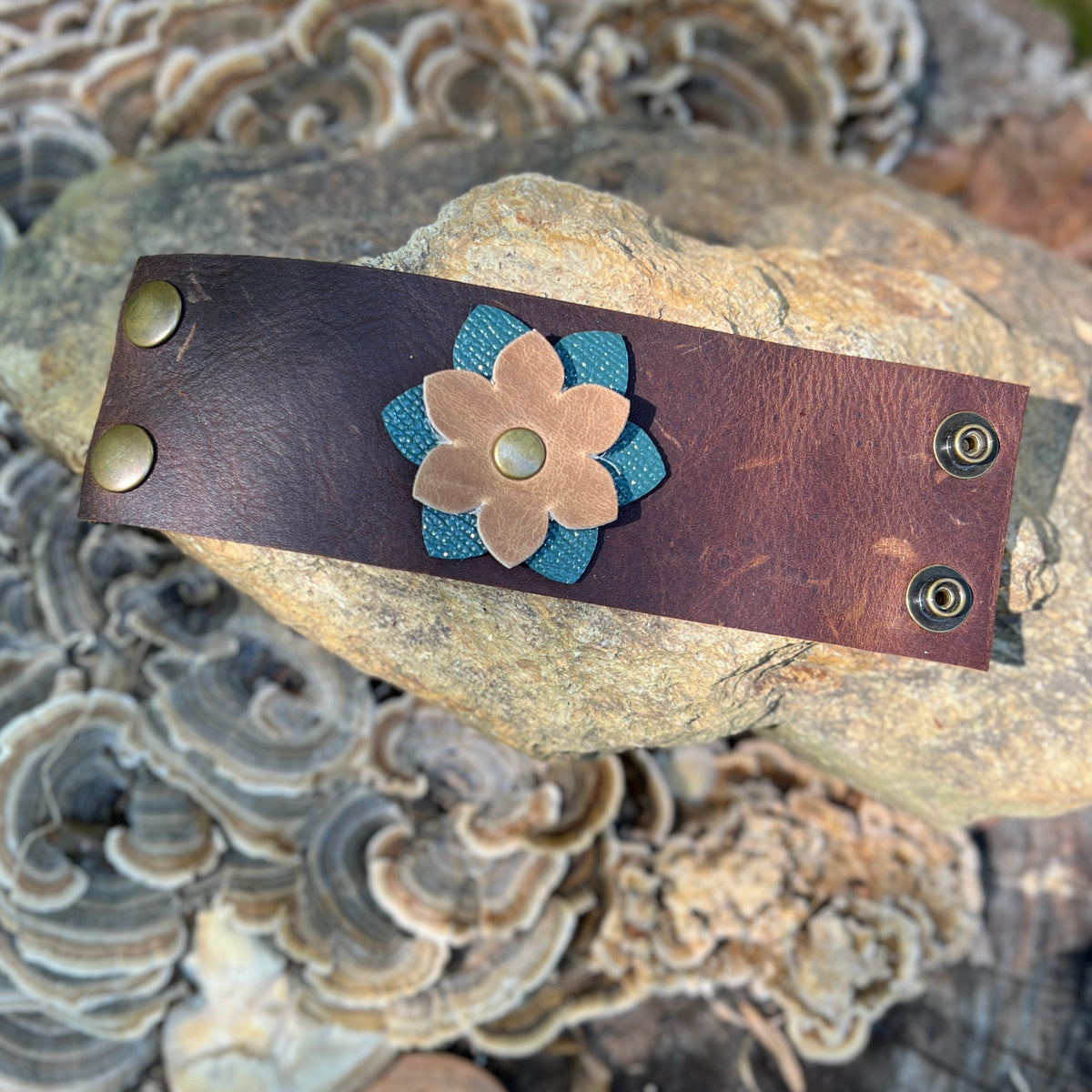 leather scarf cuff with flower on plaid flannel scarf on stone surface