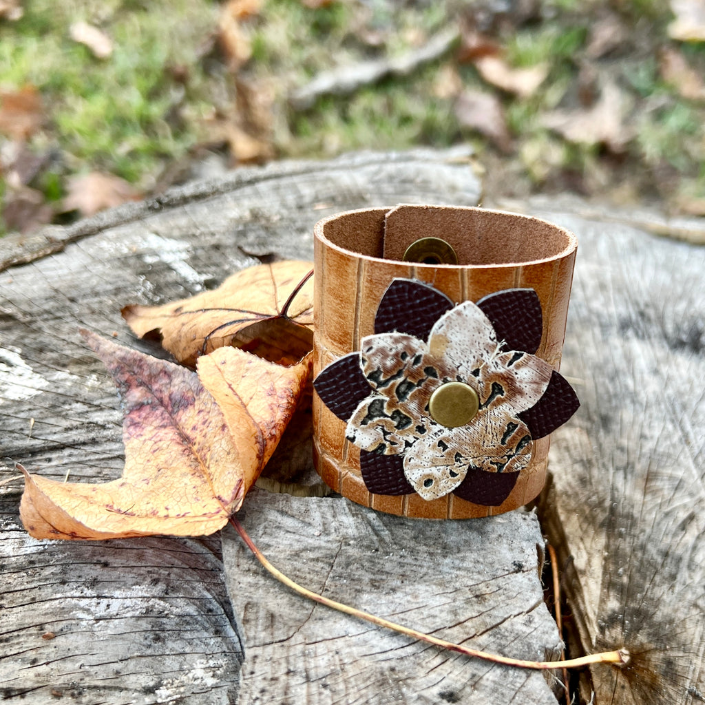 Leather cuff with floral design on a wooden surface with leaves