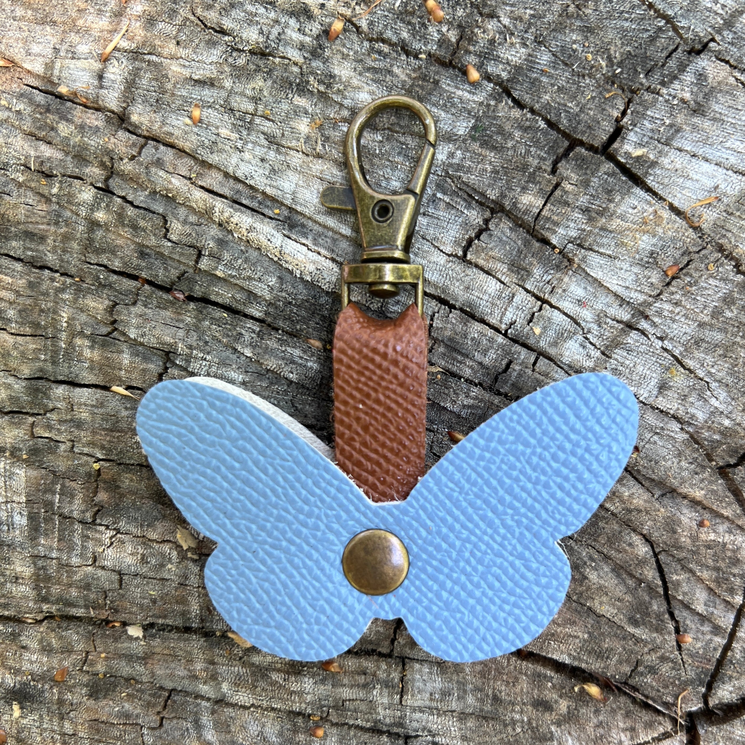 Butterfly-shaped keychain with leather strap on a wooden surface