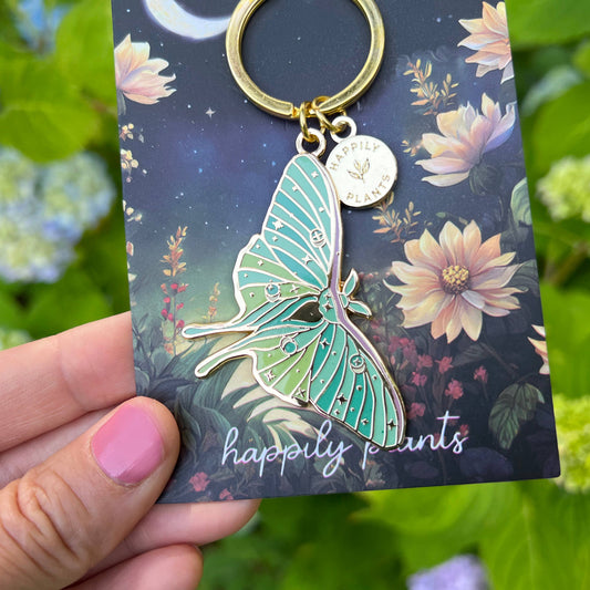 Butterfly-shaped keychain on a 'happily plants' branded card with greenery in the background