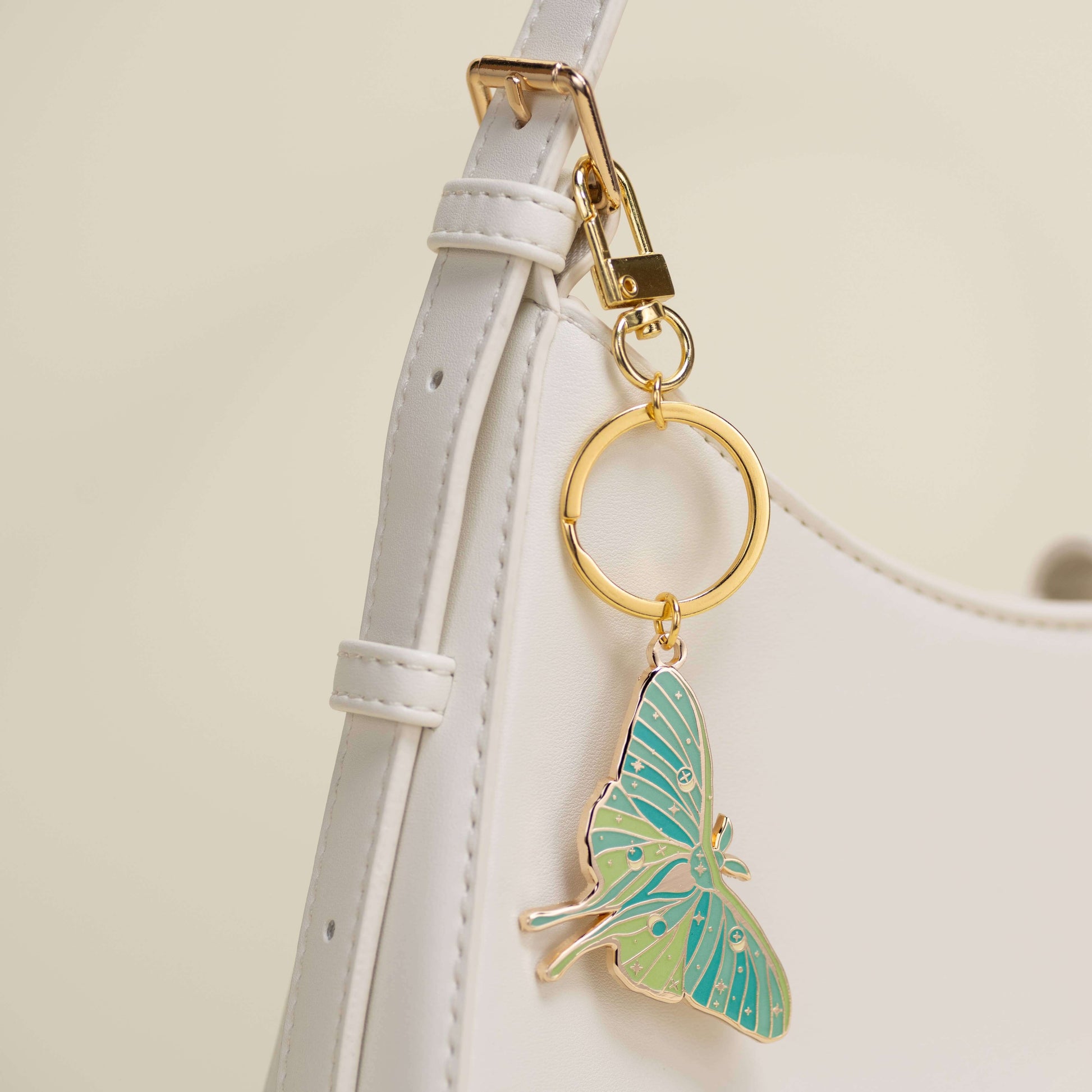 Butterfly keychain attached to a white strap with a gold ring on a light beige background