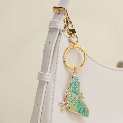 Butterfly keychain attached to a white strap with a gold ring on a light beige background